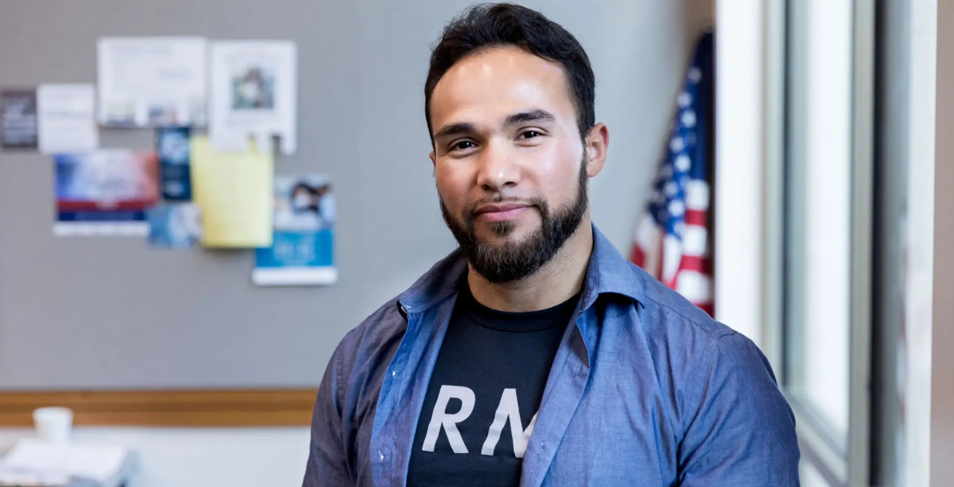Smiling bearded man by bulletin board and flag