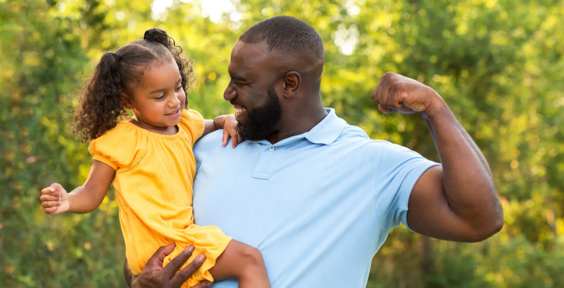 Man holding smiling girl, flexing arm outdoors