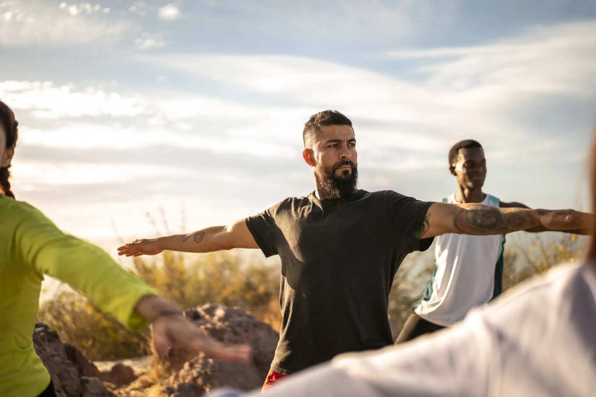 Group practicing outdoor yoga with outstretched arms