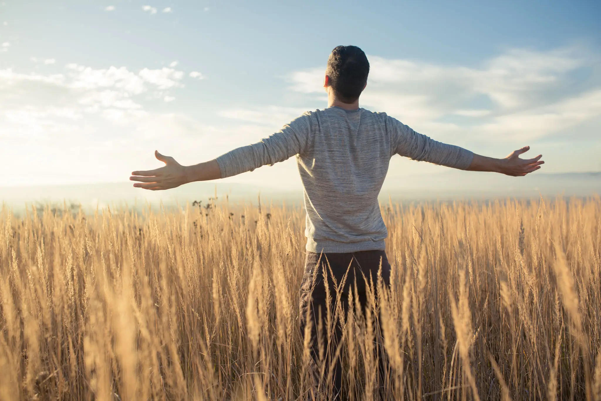 Man standing in wheat field with arms outstretched