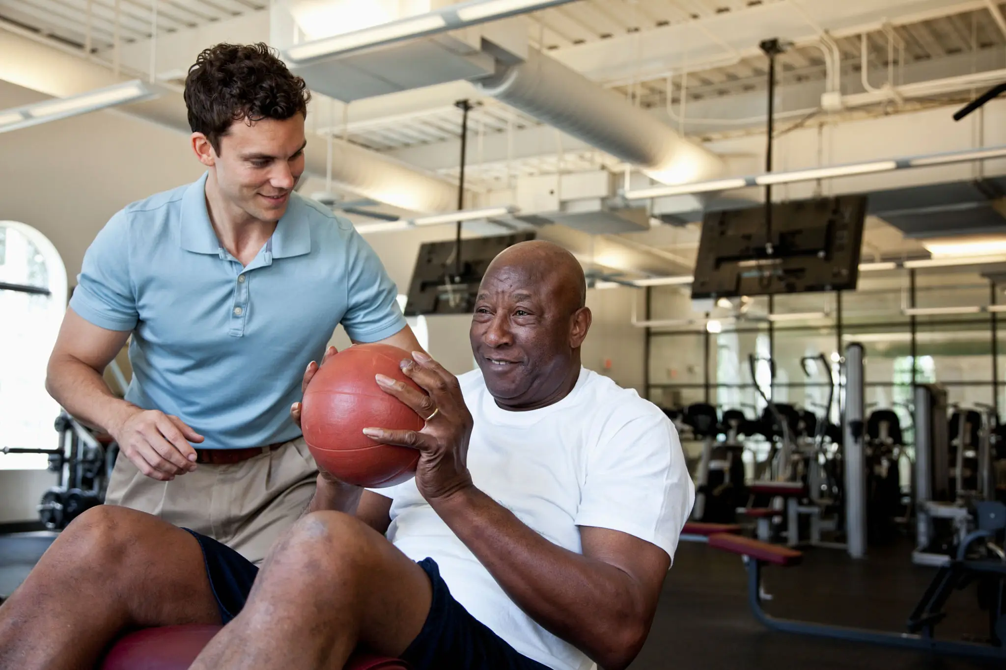 Personal trainer helps senior with medicine ball