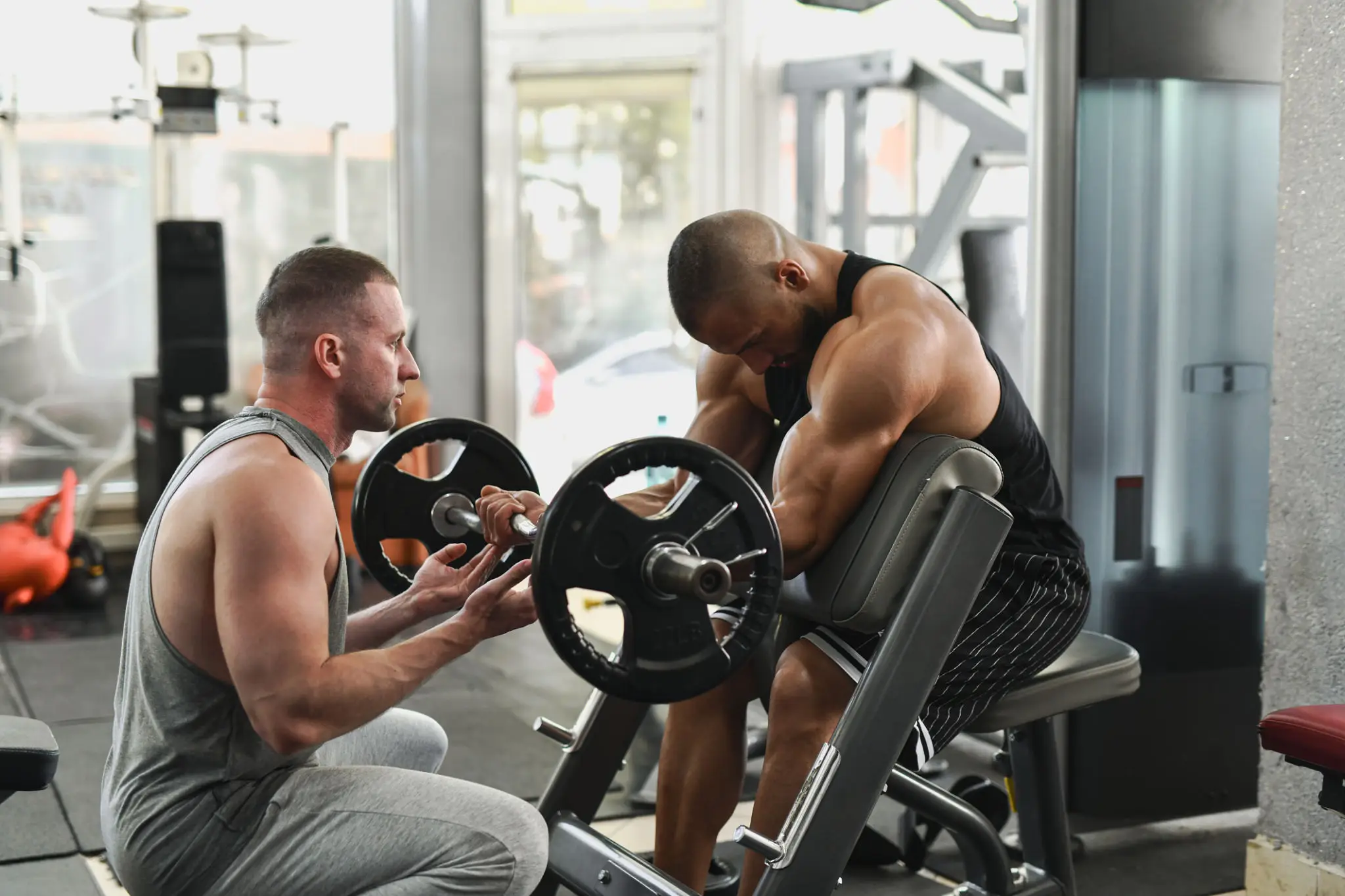 Trainer spotting man doing preacher curls