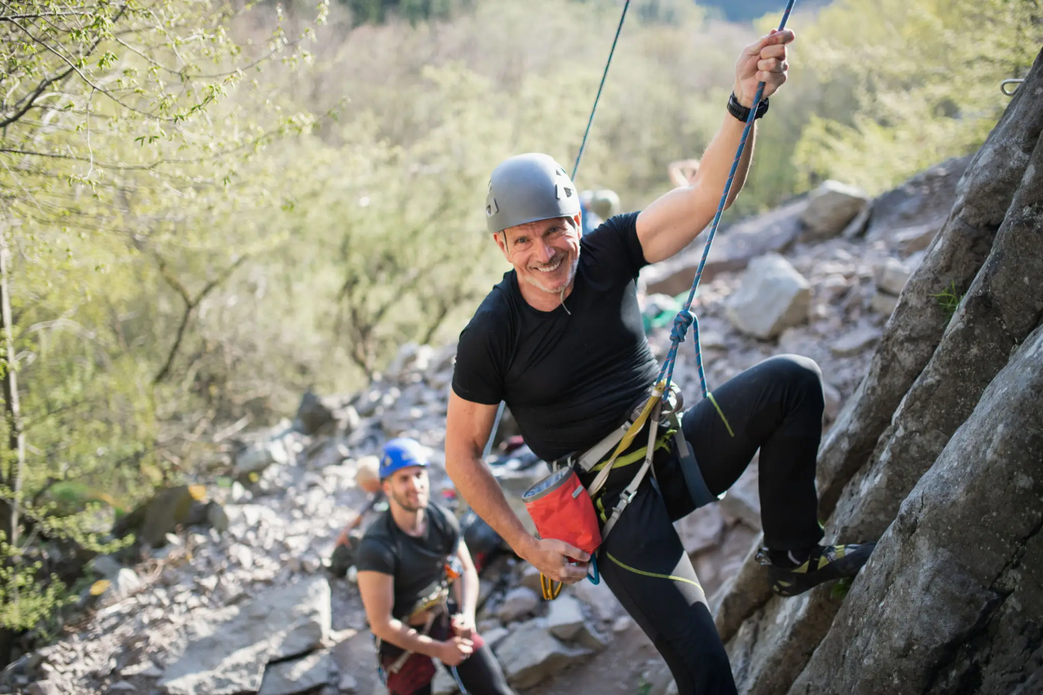 Smiling climber ascending rock with partner belaying