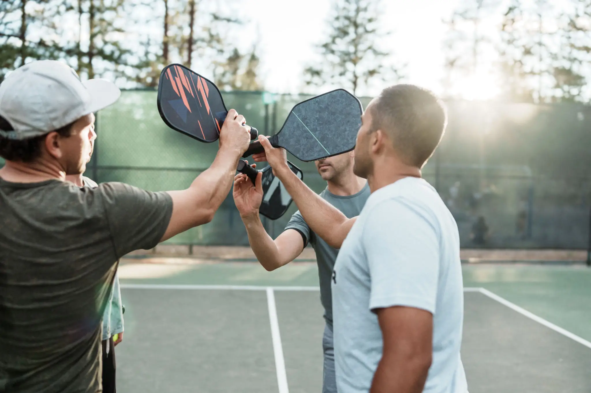 Three players bumping paddles on pickleball court