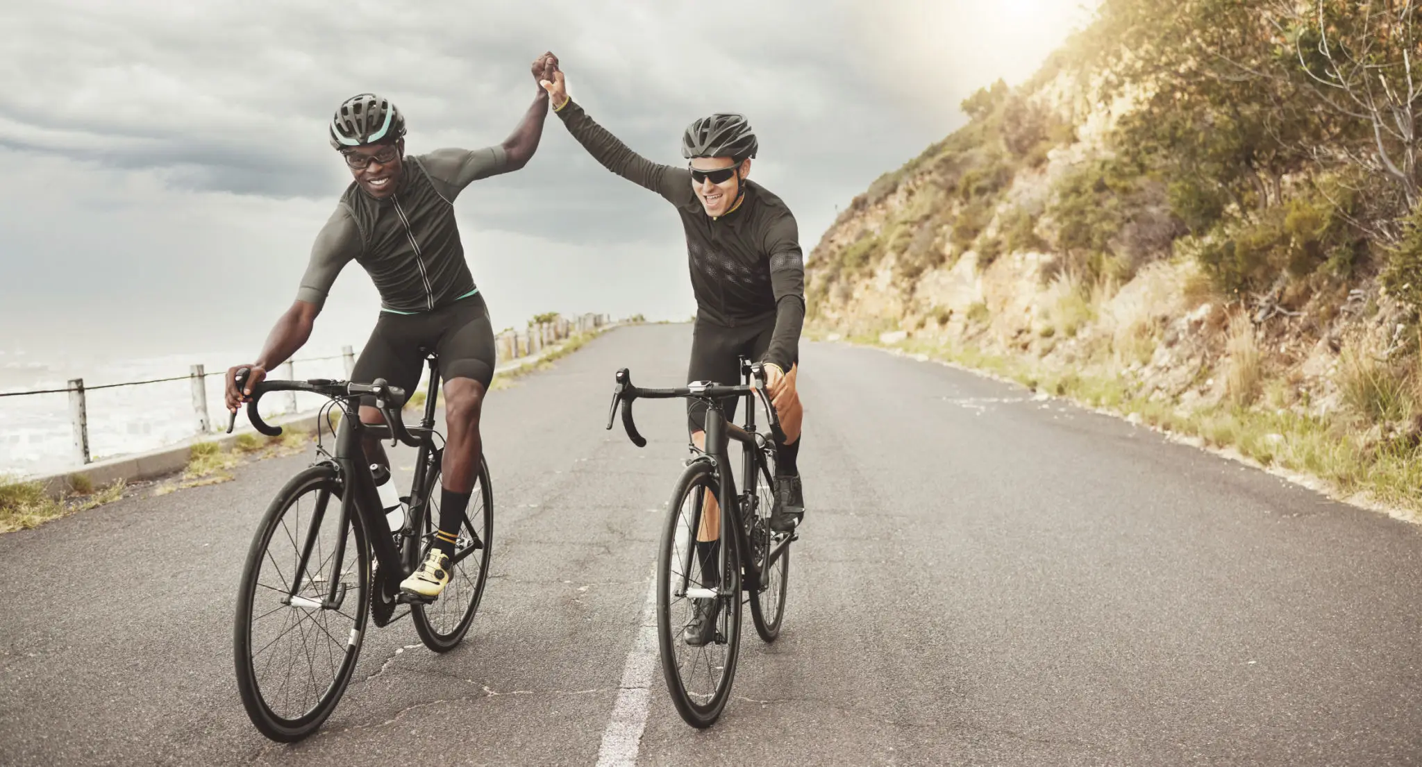 Two cyclists high-fiving on coastal road