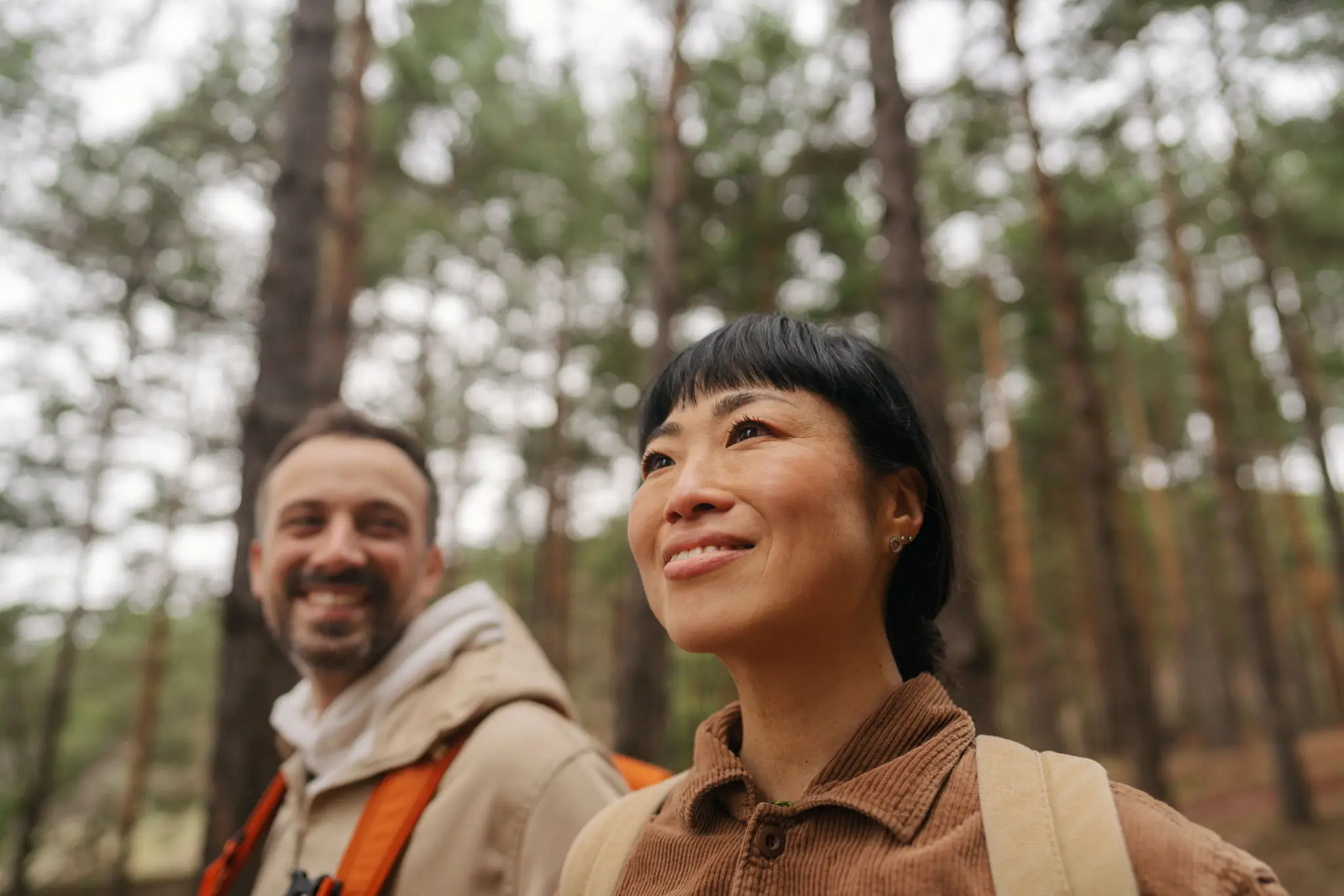 Two smiling hikers with backpacks in pine forest