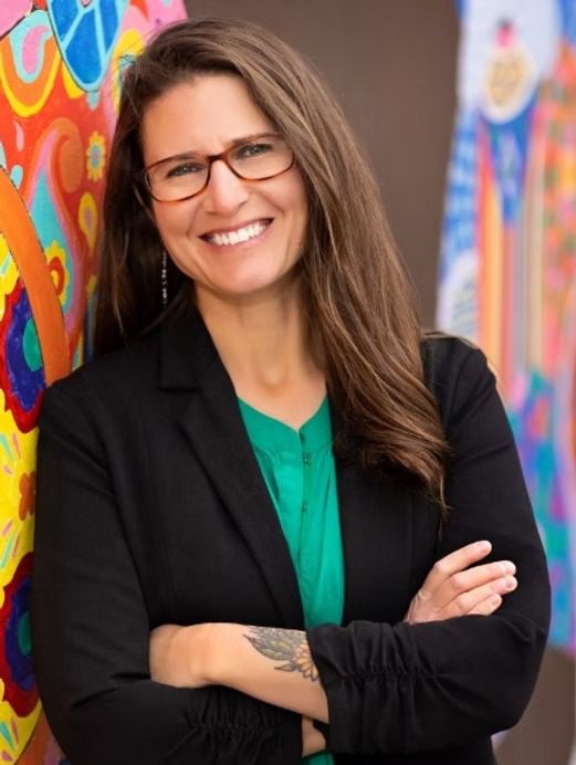 Smiling woman with glasses by colorful mural