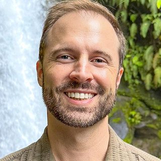 Smiling bearded man by waterfall and greenery
