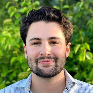Smiling young man headshot outdoors with foliage