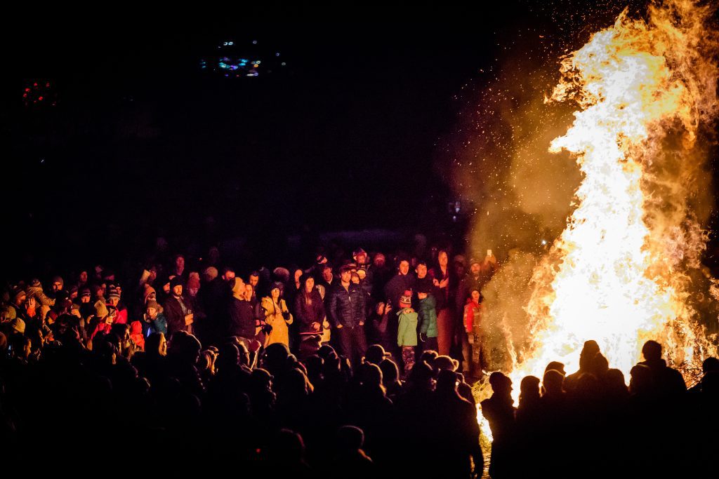 Large crowd gathered around roaring bonfire
