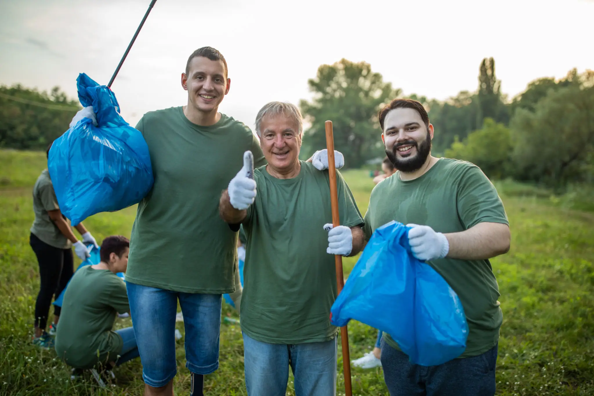 Three volunteers cleaning park holding blue trash bags
