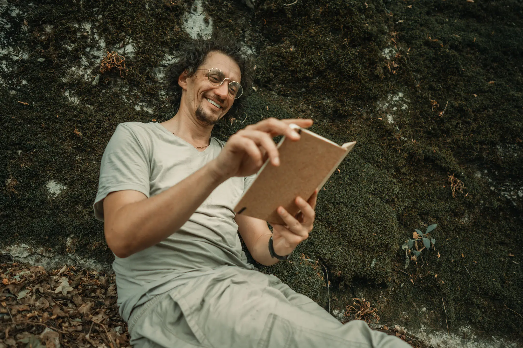 Man reading notebook outdoors against mossy rock