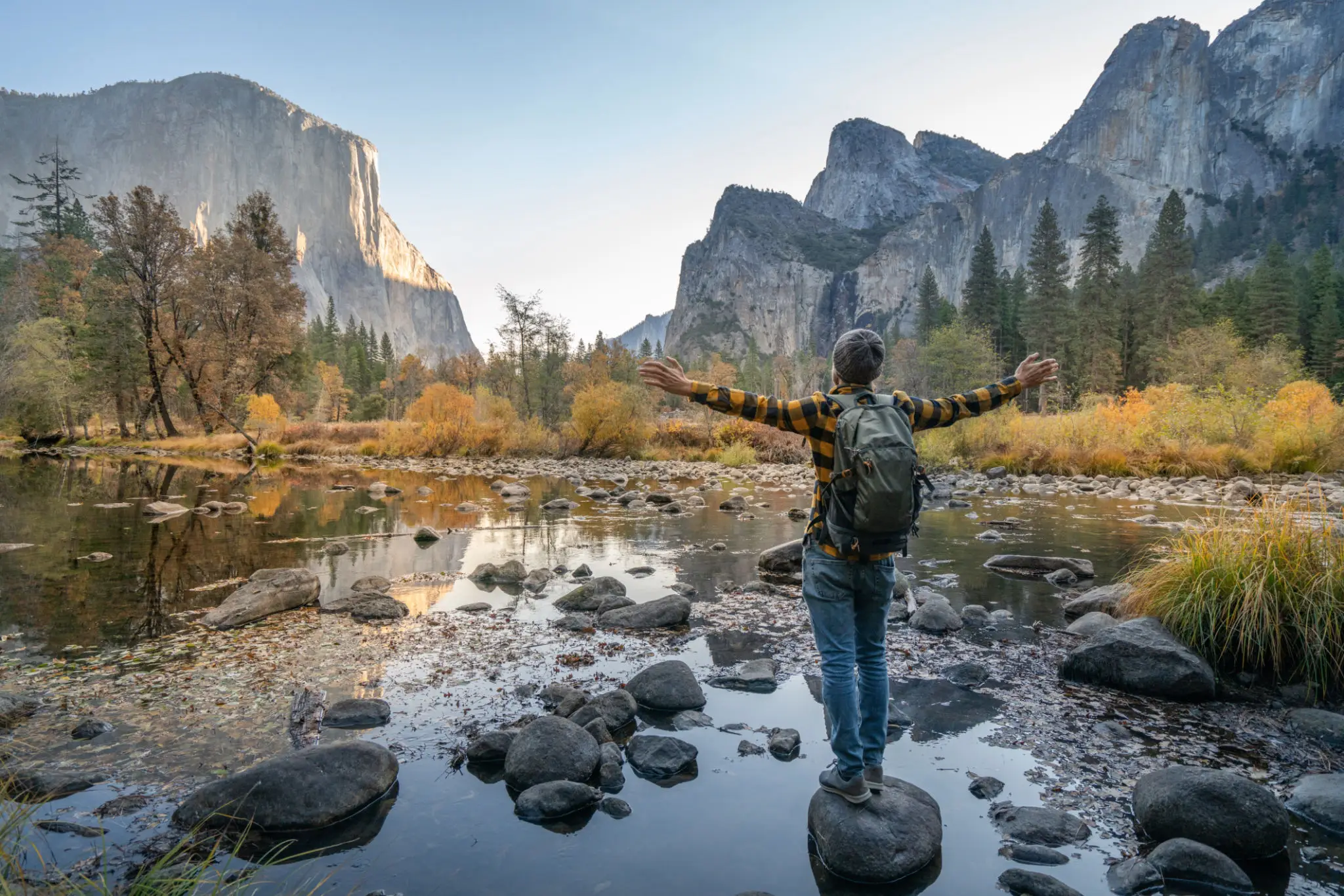 Hiker with backpack arms outstretched by river