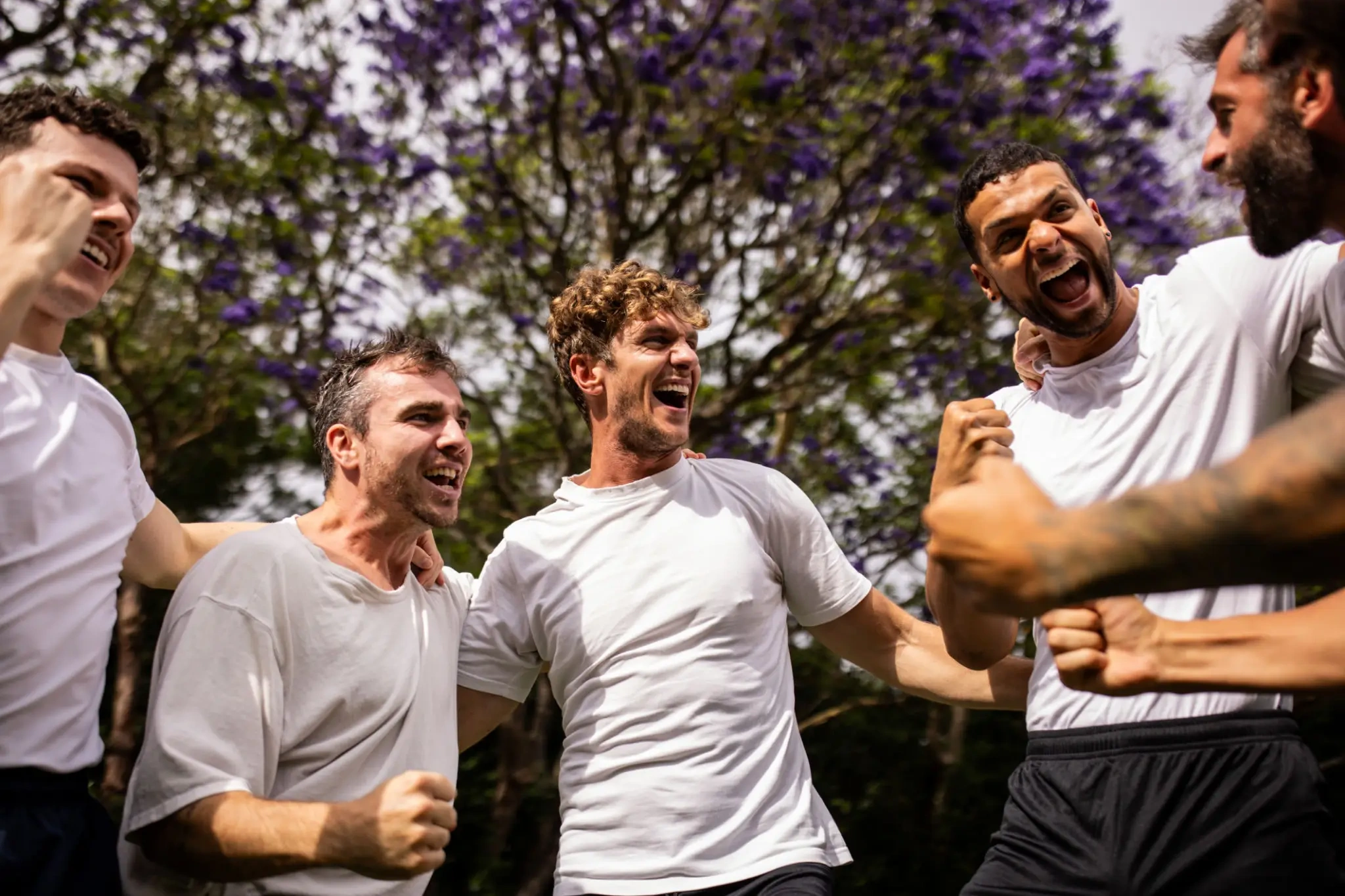 Group of men cheering outdoors under purple trees