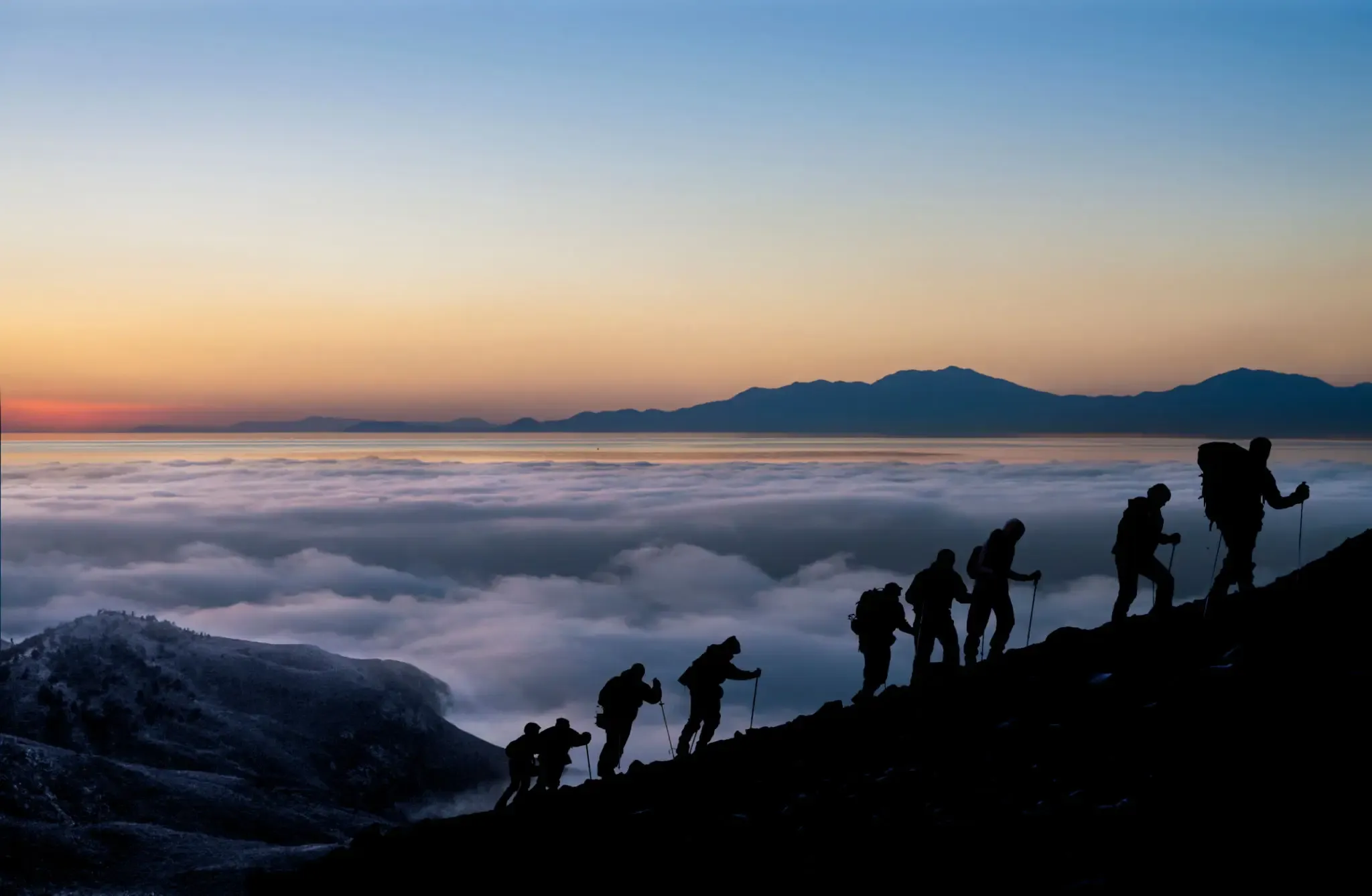Silhouetted hikers ascending mountain above cloud sea