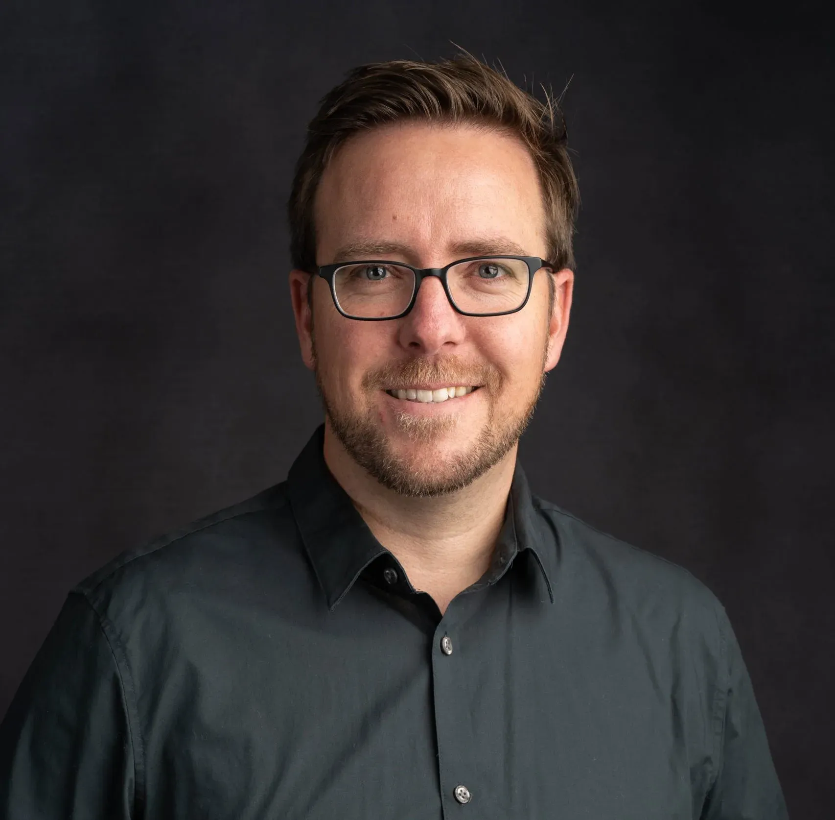 Smiling man with glasses in dark shirt